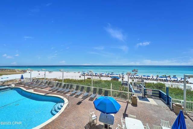 view of swimming pool featuring a patio, a water view, and a view of the beach