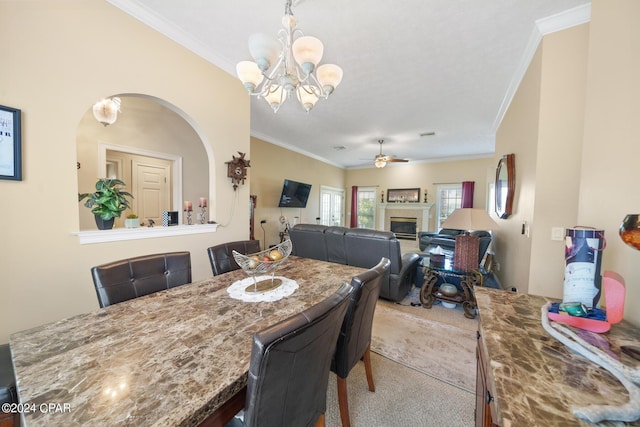 carpeted dining space featuring a glass covered fireplace, crown molding, and ceiling fan with notable chandelier