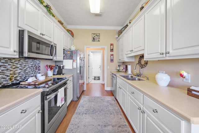 kitchen with sink, stainless steel appliances, ornamental molding, white cabinets, and light wood-type flooring