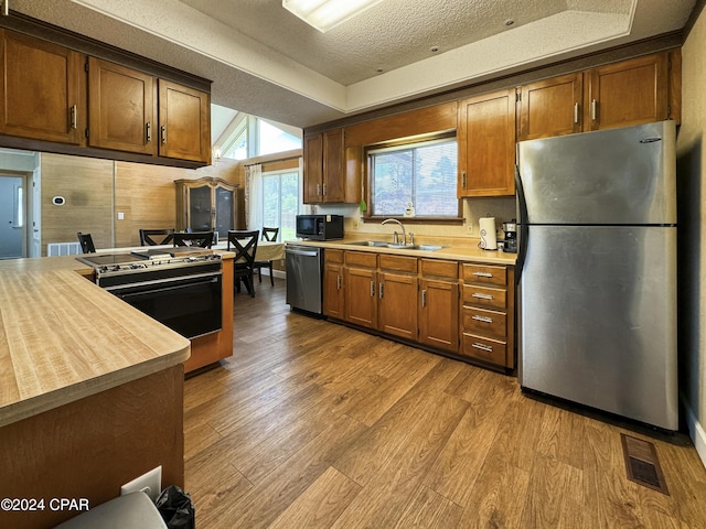 kitchen featuring sink, light hardwood / wood-style flooring, a textured ceiling, appliances with stainless steel finishes, and a tray ceiling