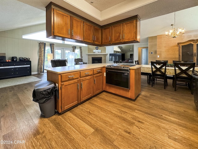 kitchen featuring kitchen peninsula, light wood-type flooring, a textured ceiling, decorative light fixtures, and a notable chandelier