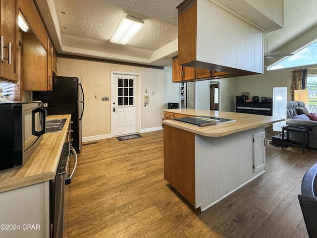 kitchen featuring cooktop, butcher block countertops, kitchen peninsula, light hardwood / wood-style floors, and a textured ceiling