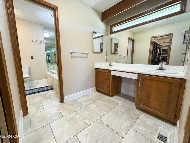 bathroom featuring vanity, toilet, a textured ceiling, and tiled bath