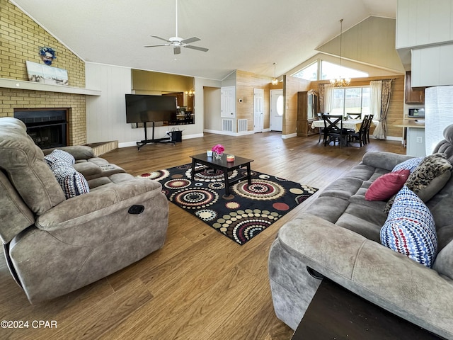 living room with a fireplace, ceiling fan with notable chandelier, wood-type flooring, and vaulted ceiling