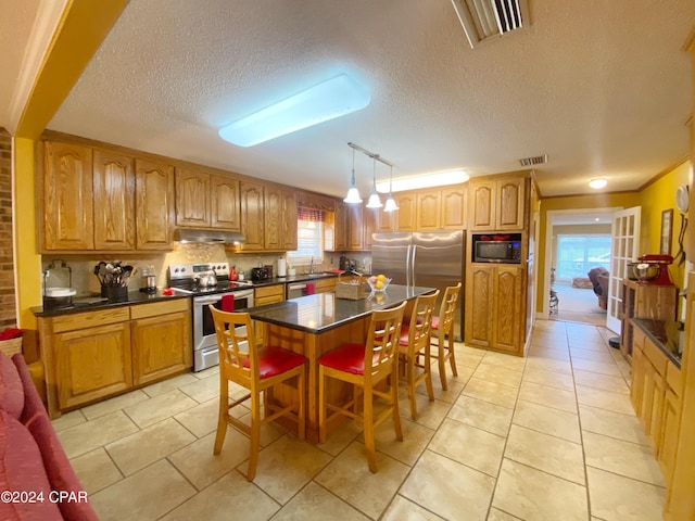 kitchen with stainless steel appliances, a center island, light tile flooring, and decorative light fixtures