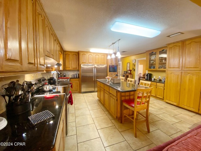 kitchen with a center island, a textured ceiling, stainless steel refrigerator, and light tile floors