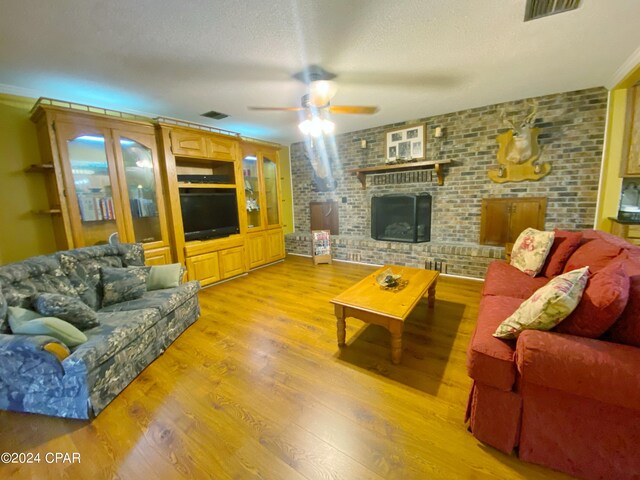 living room featuring light hardwood / wood-style floors, a textured ceiling, brick wall, a fireplace, and ceiling fan