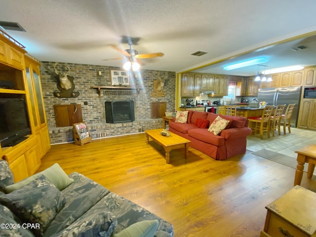 living room with ceiling fan, light hardwood / wood-style flooring, a fireplace, a textured ceiling, and brick wall