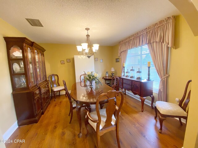 dining space with an inviting chandelier, a textured ceiling, and hardwood / wood-style flooring