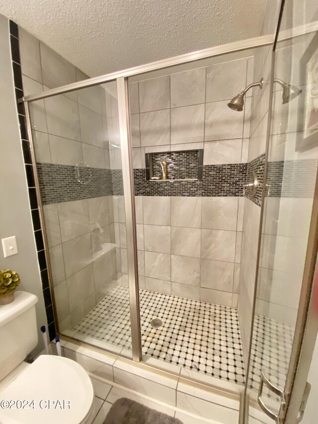 bathroom with tile floors, a shower with door, toilet, and a textured ceiling