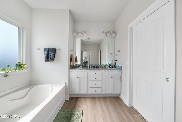 bathroom with dual vanity, a tub to relax in, and hardwood / wood-style flooring