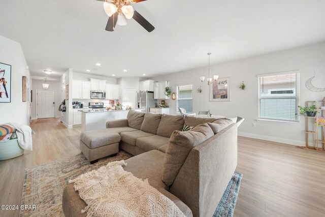 living room with ceiling fan with notable chandelier, a healthy amount of sunlight, and light wood-type flooring