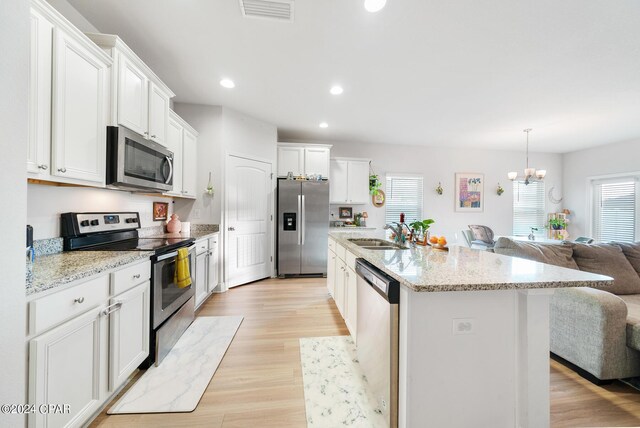 kitchen featuring stainless steel appliances, white cabinets, sink, a center island with sink, and light hardwood / wood-style floors