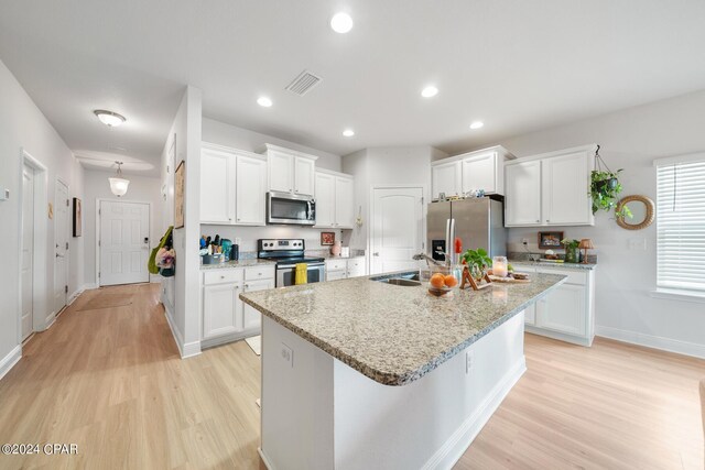 kitchen with white cabinetry, stainless steel appliances, light hardwood / wood-style flooring, and a center island with sink