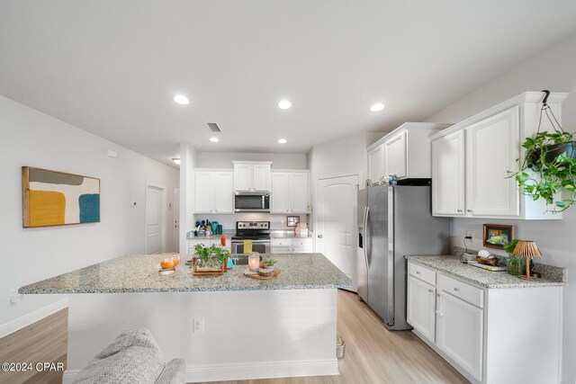 kitchen with appliances with stainless steel finishes, light hardwood / wood-style flooring, white cabinetry, and a kitchen island with sink