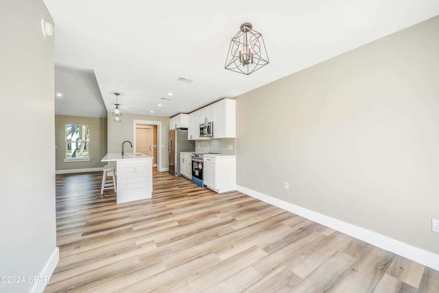 kitchen with stainless steel appliances, a center island with sink, a kitchen bar, and decorative light fixtures