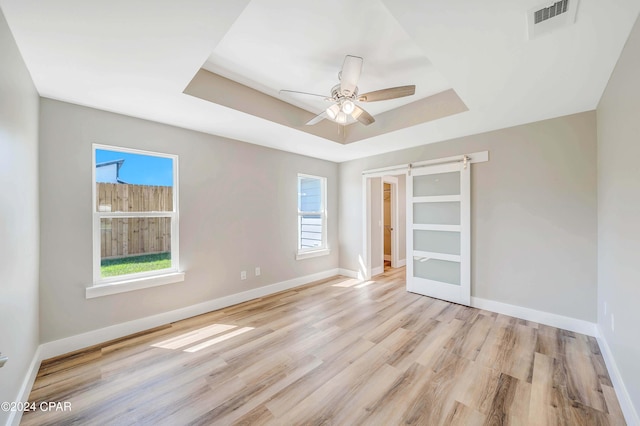 interior space with multiple windows, a tray ceiling, light hardwood / wood-style flooring, and a barn door