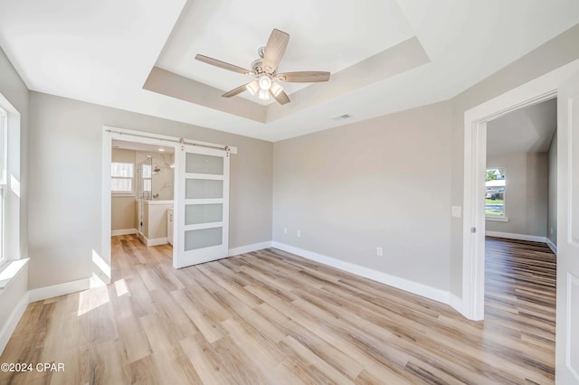 interior space featuring a raised ceiling, a barn door, ceiling fan, and light hardwood / wood-style floors