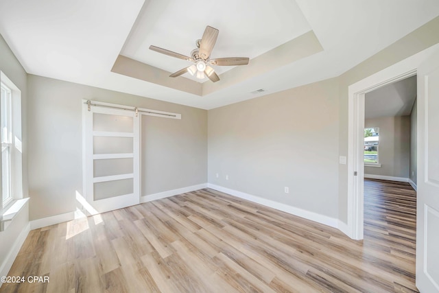 spare room with ceiling fan, a barn door, a raised ceiling, and light hardwood / wood-style flooring