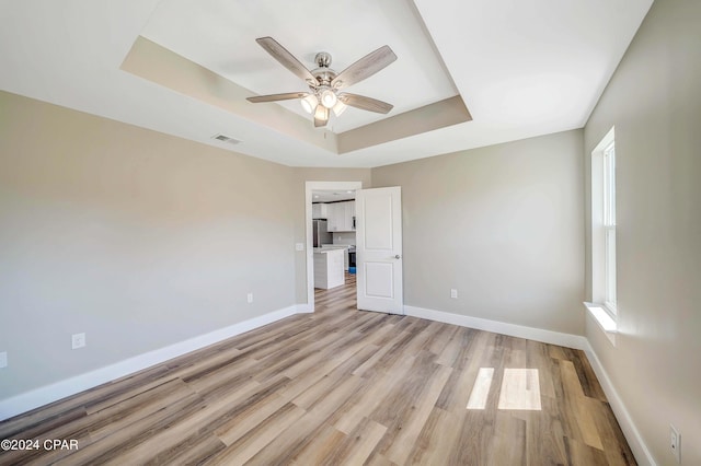 spare room with a barn door, a tray ceiling, light hardwood / wood-style flooring, and ceiling fan