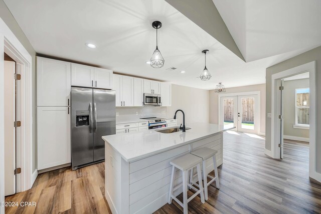 kitchen featuring a kitchen island with sink, white cabinets, sink, stainless steel dishwasher, and light hardwood / wood-style floors