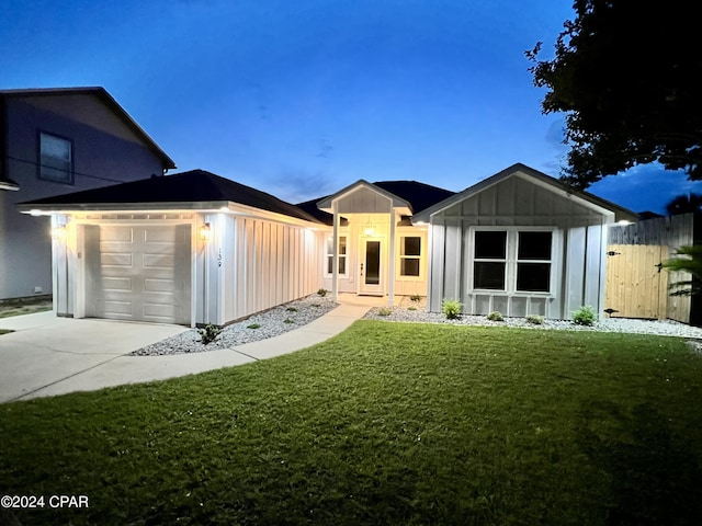 back house at dusk featuring a garage and a lawn