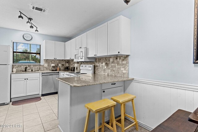 kitchen with a breakfast bar, white appliances, kitchen peninsula, light stone countertops, and white cabinetry