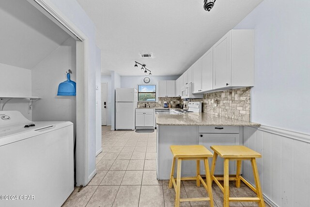 kitchen featuring a kitchen breakfast bar, light stone counters, white appliances, washer / dryer, and white cabinets