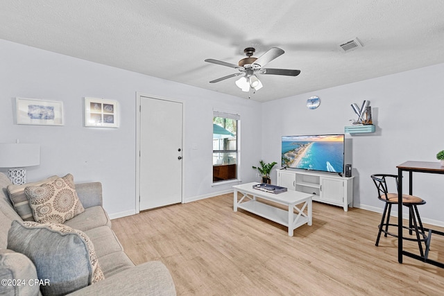 living room with a textured ceiling, light wood-type flooring, and ceiling fan