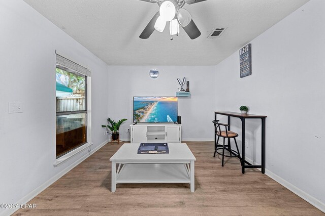 living room with ceiling fan, a textured ceiling, and light hardwood / wood-style flooring