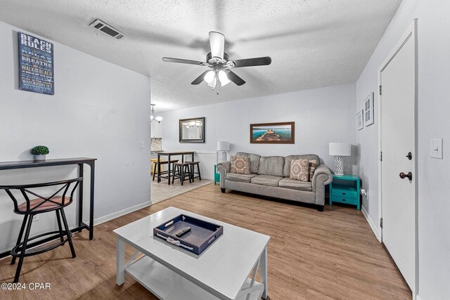 living room featuring ceiling fan with notable chandelier, a textured ceiling, and light hardwood / wood-style floors