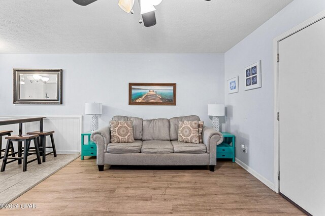 living room featuring ceiling fan, a textured ceiling, and light wood-type flooring