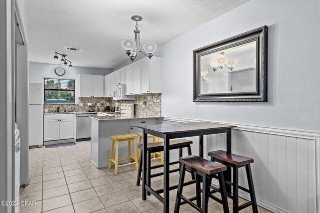 kitchen with kitchen peninsula, a textured ceiling, white appliances, white cabinetry, and a breakfast bar area