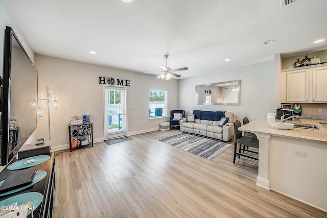 living room featuring a textured ceiling, light hardwood / wood-style flooring, ceiling fan, and sink