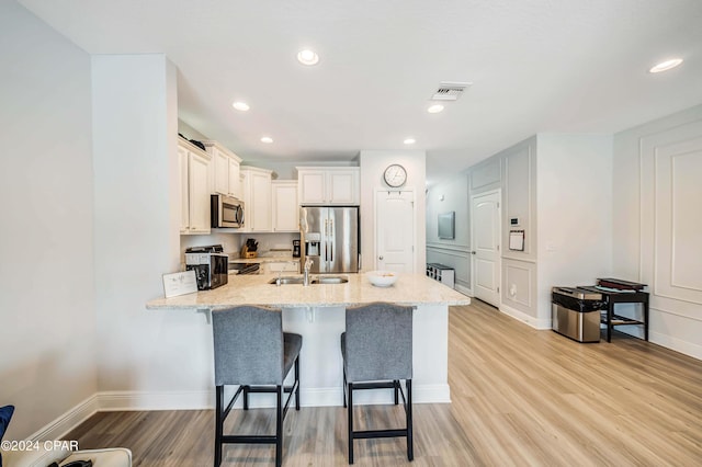 kitchen featuring a kitchen breakfast bar, light stone countertops, light wood-type flooring, and appliances with stainless steel finishes