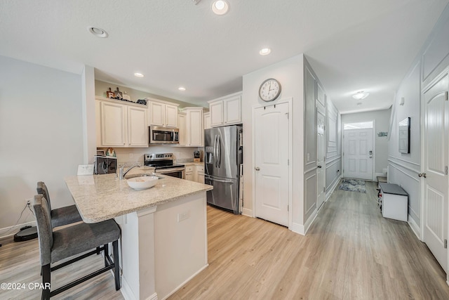 kitchen featuring kitchen peninsula, appliances with stainless steel finishes, light wood-type flooring, a kitchen breakfast bar, and sink