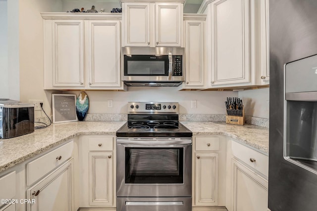 kitchen with light stone counters, cream cabinetry, and appliances with stainless steel finishes