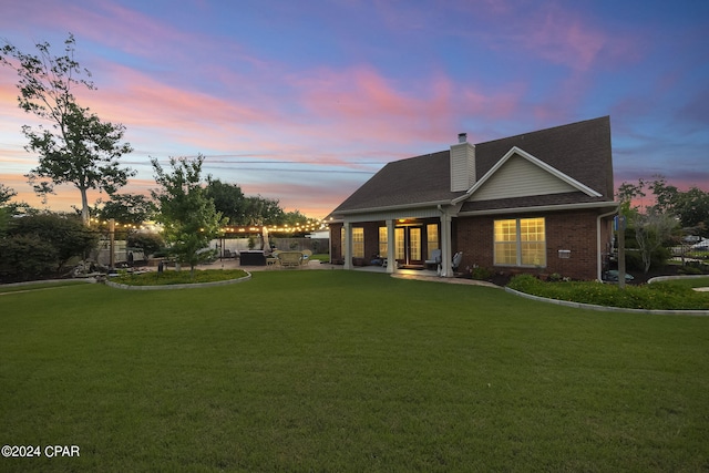 back house at dusk with a lawn and a patio area