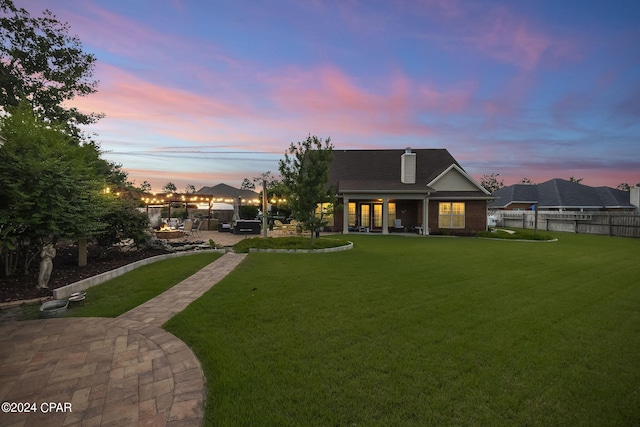 back house at dusk featuring a lawn and a patio