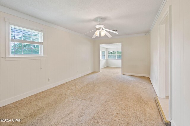 empty room with ceiling fan, a textured ceiling, ornamental molding, and light carpet