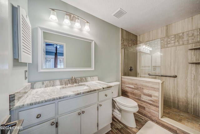 bathroom featuring a tile shower, vanity, a textured ceiling, and toilet