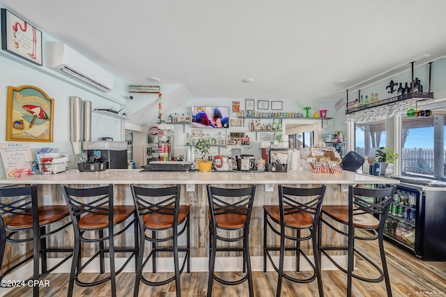 kitchen featuring kitchen peninsula, wood-type flooring, an AC wall unit, and a breakfast bar area