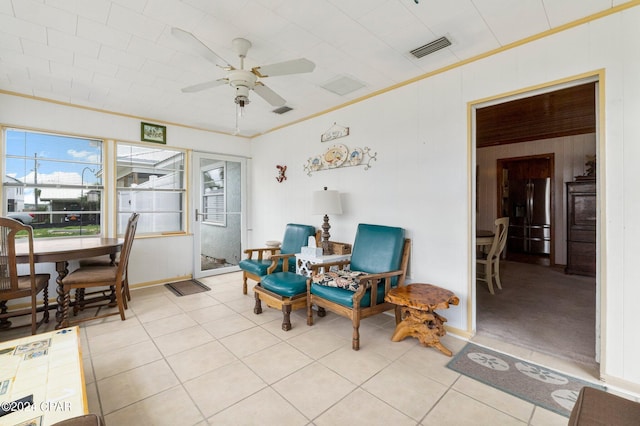 living area featuring ceiling fan, wooden walls, crown molding, and light tile patterned floors