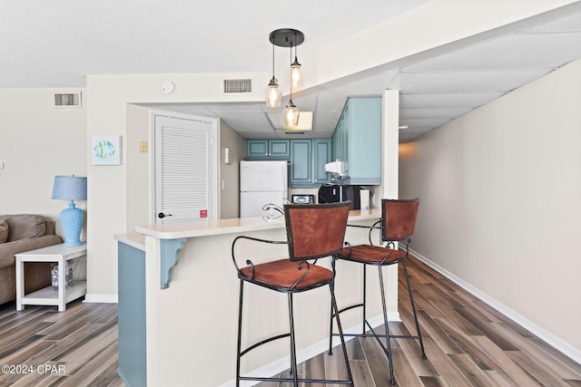 kitchen featuring white fridge, pendant lighting, kitchen peninsula, a kitchen breakfast bar, and blue cabinets