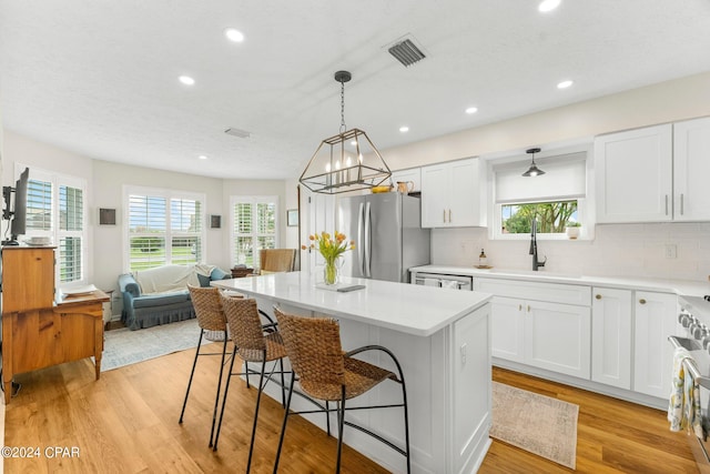 kitchen with stainless steel fridge, a kitchen island, light hardwood / wood-style flooring, backsplash, and white cabinets