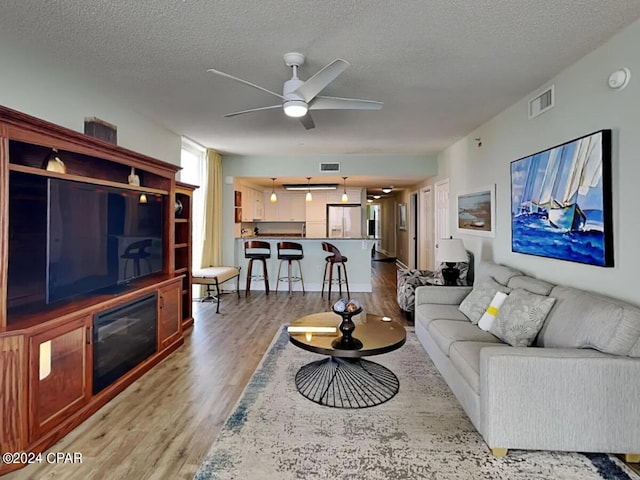 living room featuring ceiling fan, light hardwood / wood-style flooring, and a textured ceiling