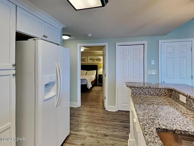 kitchen with a textured ceiling, white cabinets, light stone countertops, white refrigerator with ice dispenser, and light wood-type flooring