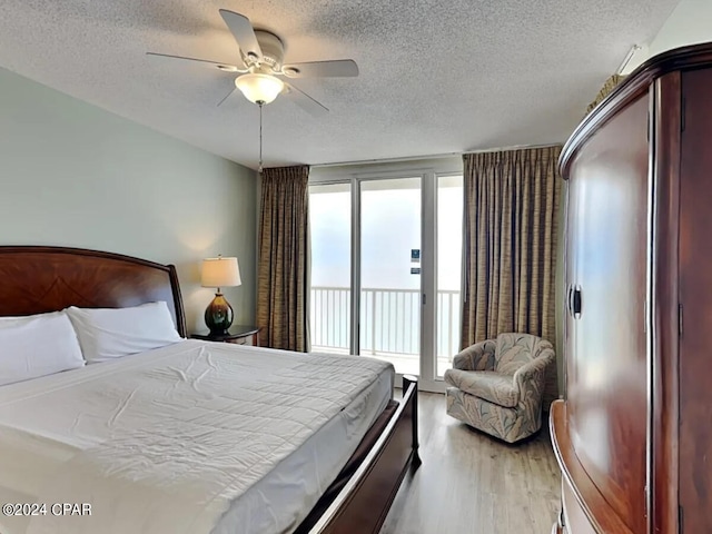 bedroom with a textured ceiling, access to outside, ceiling fan, expansive windows, and light hardwood / wood-style flooring