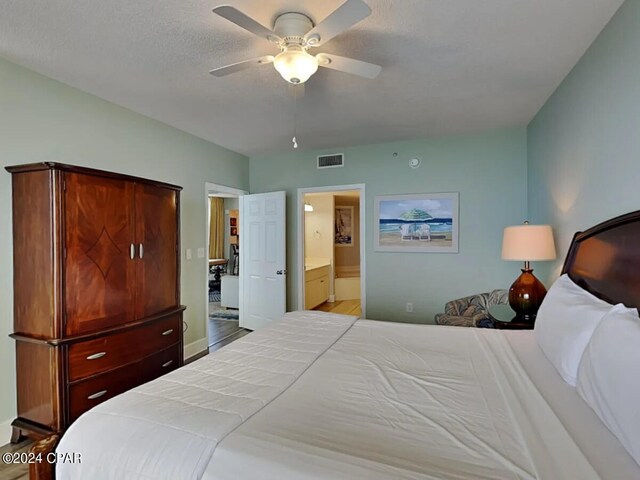 bedroom featuring ensuite bath, a textured ceiling, light wood-type flooring, and ceiling fan