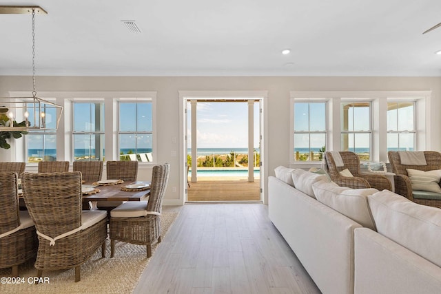 living room featuring plenty of natural light, light hardwood / wood-style floors, a water view, and an inviting chandelier